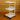 White rolling cart with three shelves on a brown floor and wall.